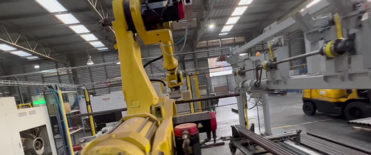Robot FANUC en una celda de mecanizado manejando barras de acero